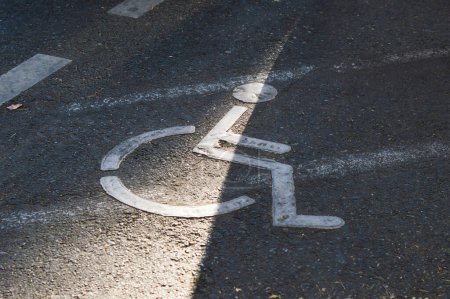 Foto de Señal de silla de ruedas blanca en un estacionamiento asfaltado, indicando lugar reservado para personas con discapacidad física - Imagen libre de derechos