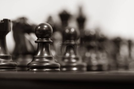 Foto de Un plano detallado de un peón negro en un enfoque agudo de pie sobre un fondo borroso de otras piezas de ajedrez. - Imagen libre de derechos