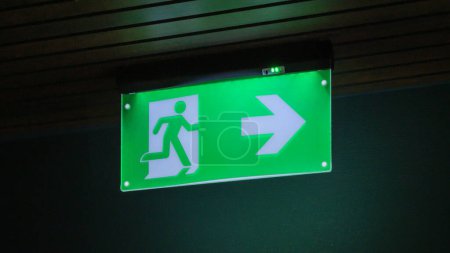 A green exit sign glowing in the darkness, indicating a way out with a rightward arrow.