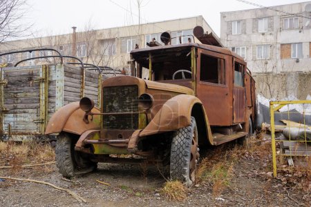 A rusty vintage Soviet truck stands abandoned by industrial buildings.