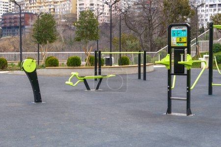 A variety of outdoor fitness machines are installed in the public park, against the residential city buildings background.