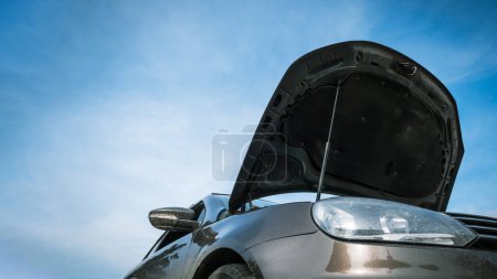 Low-angle view of open car hood against blue sky background with copy space.