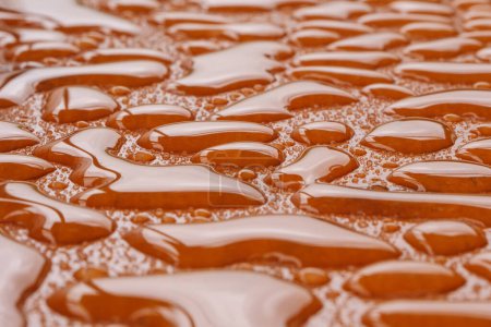 Les gouttelettes liquides sont réparties sur une surface de couleur orange, créant un fond de texture macro unique, tourné avec une faible profondeur de champ.
