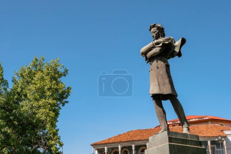 Foto de The statue of Georgian poet Nikoloz Baratashvili stands prominently against the backdrop of old Tbilisi houses and green trees under a clear blue sky. Tbilisi, Georgia - May 17, 2024. - Imagen libre de derechos