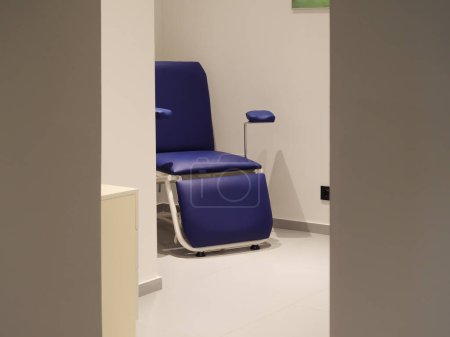Una silla médica azul se coloca en una sala de la clínica limpia y vacía. La iluminación es brillante, y el medio ambiente parece estéril y profesional.