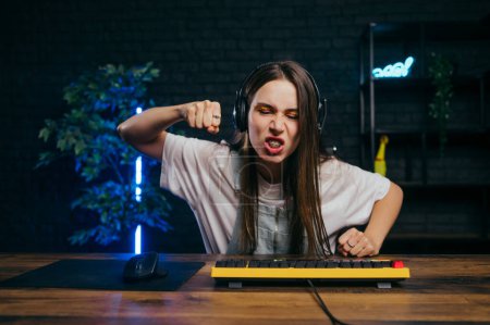 Photo for Angry female gamer in headphones lost the game and screams and shows her fist to the camera - Royalty Free Image