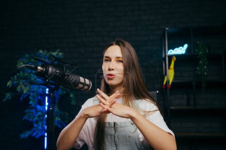 Photo for Positive female blogger talking into a microphone in a studio with a frown on her face looking at the camera on a dark background. - Royalty Free Image