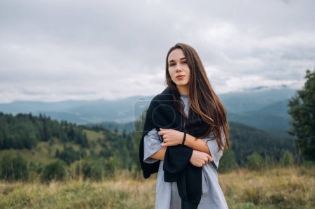 Photo for Portrait of an attractive female tourist in casual clothes standing in the mountains with a serious face on posing for the camera, resting on a hike. - Royalty Free Image
