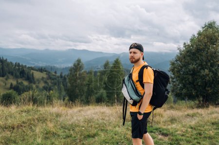 Photo for Portrait of a handsome male tourist in a beard and in casual clothes in the mountains on the background of a beautiful landscape of the Carpathian mountains is resting. - Royalty Free Image