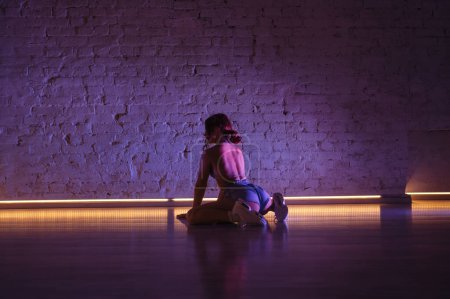 Photo for Sexy woman dancing twerk in dance studio in pink light sitting on the ground. - Royalty Free Image