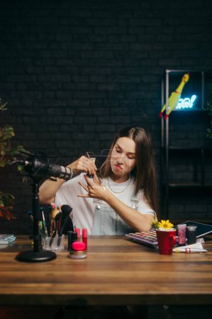 Foto de Linda señora belleza blogger está sentado en la mesa en el estudio para disparar y probar maquillaje para un cameo mientras graba una lección. - Imagen libre de derechos
