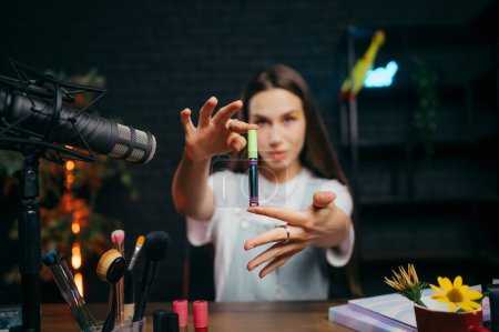 Photo for Attractive female blogger shows a tube of cosmetics to the camera and records a beauty video for social networks. The work of a beauty blogger. - Royalty Free Image