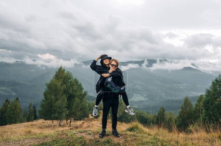 Photo for Young male tourist carries his girlfriend on his back in the mountains against the background of an unreal cloudy view. - Royalty Free Image