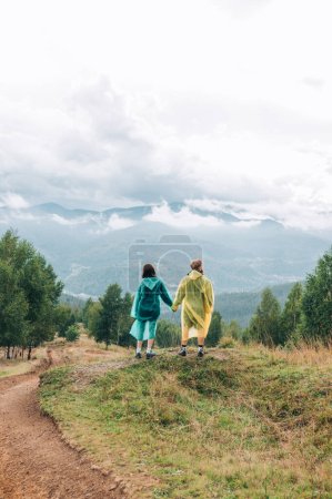 Photo for A woman and a man holding hands are standing in the mountains on the background of mountain cloudy views. - Royalty Free Image