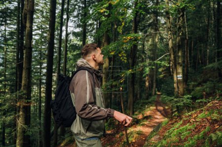 Photo for Photo of a male tourist with a stick in his hand in the mountains walking along a path and looking away. Travel in the mountains. - Royalty Free Image