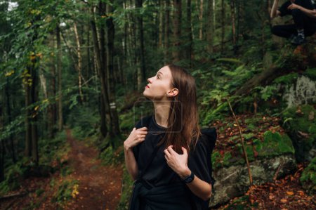 Téléchargez les photos : Randonneuse attrayant debout dans la forêt sur un sentier tout en randonnée dans les montagnes et en regardant loin avec un visage sérieux. - en image libre de droit