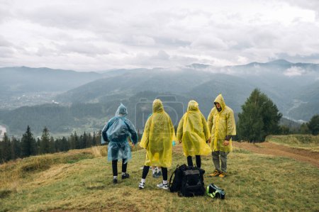 Téléchargez les photos : Un groupe de touristes en randonnée se tiennent au sommet d'une montagne et regardent vers l'avant, vue arrière sur le fond de belles vues sur les Carpates. Randonnée avec des amis dans les montagnes par temps pluvieux. - en image libre de droit