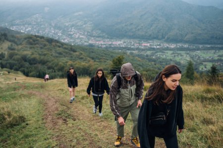Foto de Un grupo de jóvenes turistas escalan las montañas a lo largo de un sendero sobre el fondo de hermosas vistas. Turismo en los Cárpatos. Viaje de amigos a las montañas. - Imagen libre de derechos