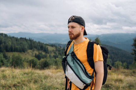 Téléchargez les photos : Beau jeune touriste masculin barbu en randonnée, portrait rapproché sur fond de belles montagnes des Carpates, détournant les yeux avec un visage sérieux. - en image libre de droit