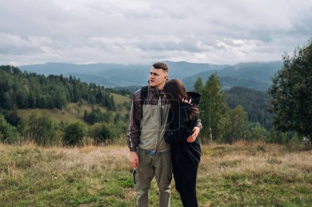 Téléchargez les photos : Un beau couple de touristes debout dans les montagnes pendant une randonnée et s'embrassant, regardant loin sur le fond de beaux paysages. - en image libre de droit