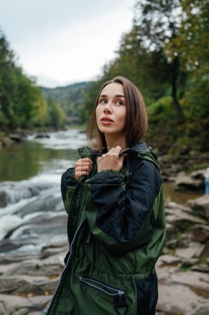 Foto de Retrato de una turista con ropa casual en una caminata posando para la cámara sobre el fondo de un río de montaña y un bosque. Recreación. - Imagen libre de derechos