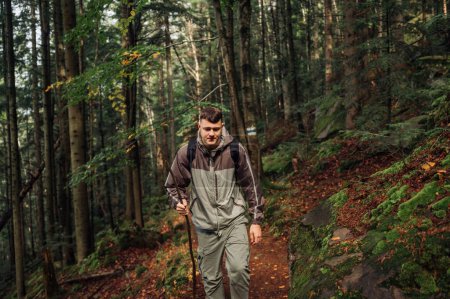 Téléchargez les photos : Un jeune homme sérieux en randonnée se promène le long d'un sentier dans une forêt vierge et regarde ses pieds. Tourisme en montagne concept. - en image libre de droit