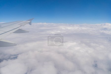 Photo for Wing of an airplane jet flying above clouds with blue sky from the window in traveling and transportation concept. Nature landscape background. - Royalty Free Image
