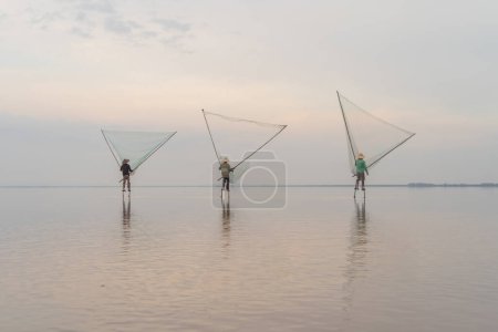 Foto de Silueta de pescador vietnamita sosteniendo una red para la captura de peces de agua dulce en la naturaleza lago o río con reflexión en la mañana en Asia en Vietnam. Gente. - Imagen libre de derechos