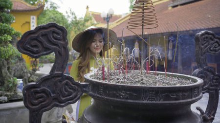 Foto de Retrato de mujer vietnamita asiática con vestido de Vietnam y sombrero de paja rezando por incienso en un templo. - Imagen libre de derechos
