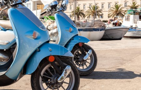 Two blue motor scooters mopeds or motorbikes in a Mediterranean fishing village harbor