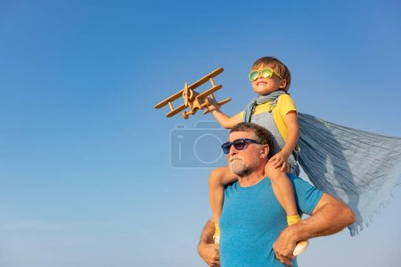 Foto de Hombre mayor y niño jugando al aire libre contra el fondo del cielo de verano. Abuelo y chico divirtiéndose juntos. Concepto de vacaciones familiares. Feliz día de los padres - Imagen libre de derechos