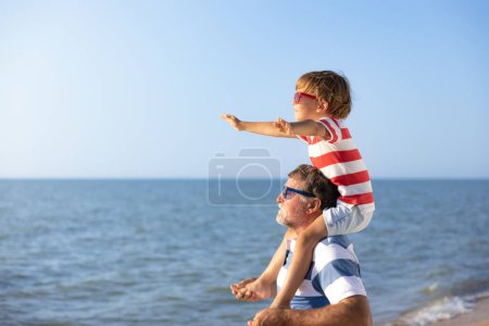Téléchargez les photos : Bonne famille s'amuser sur la plage. Grand-père et garçon sur fond bleu mer et ciel. Vacances d'été et concept de jour des pères - en image libre de droit