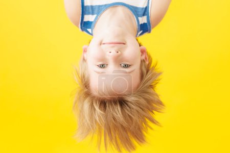 Happy child smiling against yellow paper background. Funny kid hanging upside down. Summer vacation and travel concept
