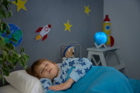 Téléchargez les photos : Joyeux enfant dormant avec une fusée et un ours en peluche. Il fait semblant d'être astronaute. Imagination et enfants rêvent concept - en image libre de droit