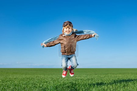 Téléchargez les photos : Joyeux enfant sautant dehors dans le champ vert printanier. Le gamin s'amuse sur fond bleu ciel. Concept d'imagination et de liberté - en image libre de droit