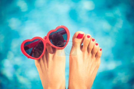 Photo for Womens feet with red pedicure against blue water background. Summer vacation concept - Royalty Free Image