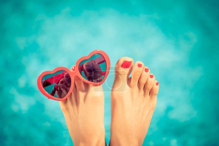 Womens feet with red pedicure against blue water background. Summer vacation concept