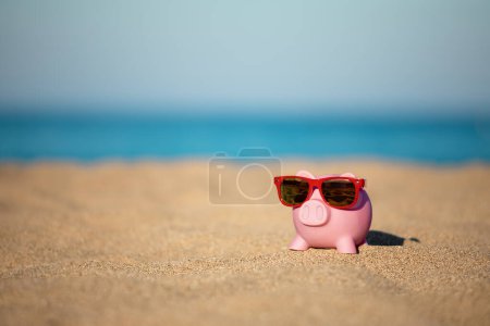 Sparschwein am Strand vor Meer und Himmel Hintergrund. Einsparungen bei Sommerreisen und Urlaubskonzept