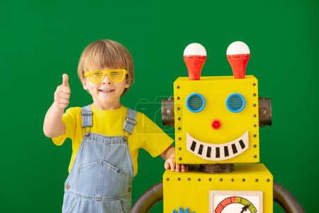 Foto de Niño feliz con robot de juguete en la escuela. Chico gracioso contra pizarra verde. Concepto de tecnología educativa, creativa e innovadora - Imagen libre de derechos