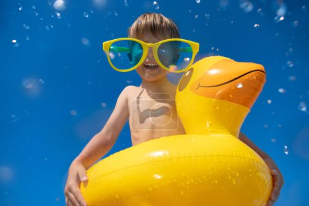 Photo for Happy child having fun on summer vacation. Funny kid jumping in swimming pool. Low angle view portrait of boy against water splash. Spring break! - Royalty Free Image