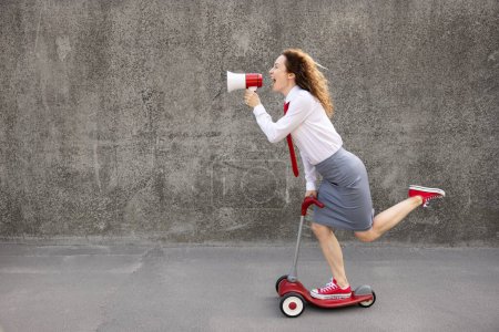 Photo for Happy businesswoman riding scooter. Outdoor portrait of young woman shouting through loudspeaker. Back to work, start up and business idea concept - Royalty Free Image