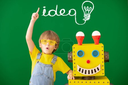 Téléchargez les photos : Enfant heureux avec robot jouet à l'école. Drôle de gamin contre le tableau vert. Éducation, créativité et innovation concept technologique - en image libre de droit