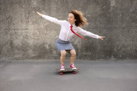 Téléchargez les photos : Heureuse femme d'affaires en skateboard. Portrait extérieur de jeune femme. Retour au travail, démarrage et concept d'idée d'entreprise - en image libre de droit