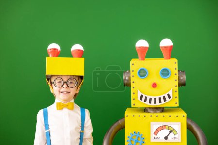 Foto de Niño feliz con robot de juguete en la escuela. Chico gracioso contra pizarra verde. Concepto de tecnología educativa, creativa e innovadora - Imagen libre de derechos