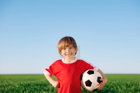 Foto de Chico feliz finge ser un jugador de fútbol. Retrato de niño al aire libre. Niño contra campo verde. Éxito y concepto ganador - Imagen libre de derechos