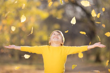 Foto de Feliz niño vomitar hojas amarillas. Niño sonriente divirtiéndose al aire libre en el parque de otoño. Concepto libertad e imaginación - Imagen libre de derechos