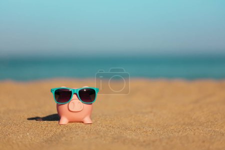 Piggybank on the beach against sea and sky background. Savings for summer travel and vacation concept