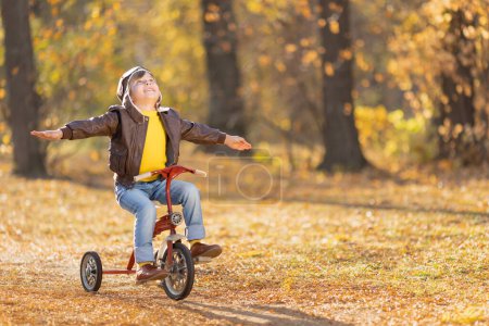 Téléchargez les photos : Portrait d'enfant pilote heureux sur fond jaune. Enfant drôle à vélo en plein air dans le parc d'automne. Concept de liberté et d'imagination - en image libre de droit
