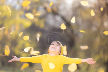 Foto de Feliz niño vomitar hojas amarillas. Niño sonriente divirtiéndose al aire libre en el parque de otoño. Concepto libertad e imaginación - Imagen libre de derechos
