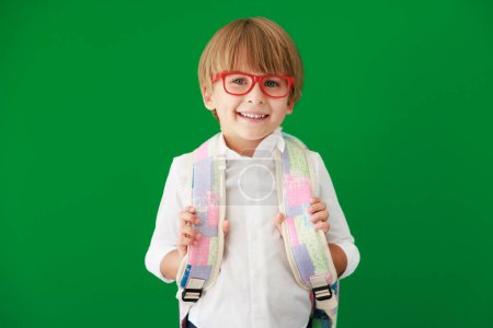 Téléchargez les photos : Enfant drôle étudiant avec sac à dos en classe. Joyeux gamin contre le tableau vert. Éducation et concept de retour à l'école - en image libre de droit